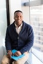 A professional black man smiling while seated by a window, embodying modern business vibes.